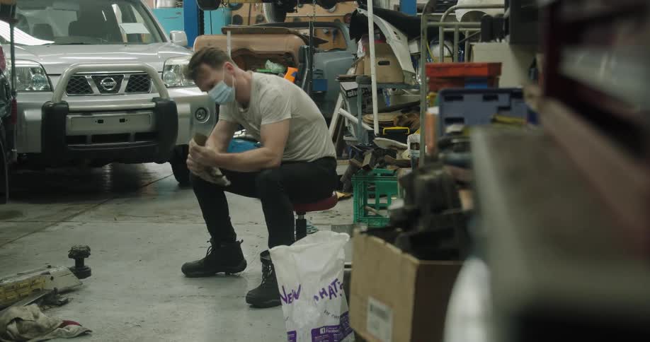 Mechanic in auto body shop sits on stool cleaning a tool