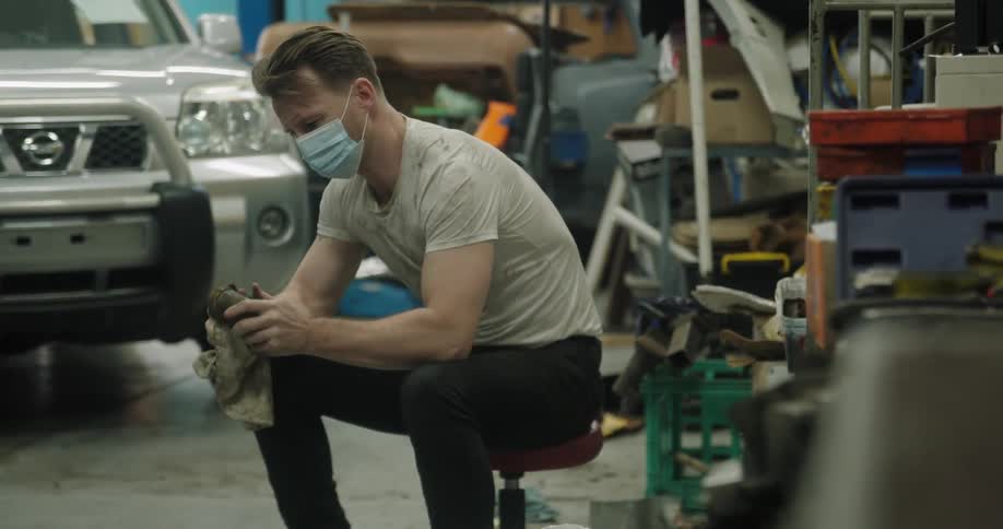 A mechanic cleans a car part sitting inside a garage