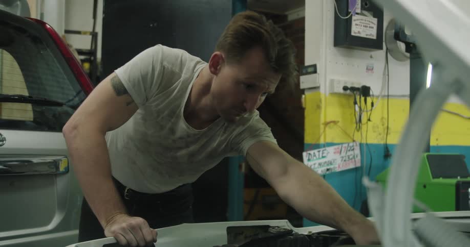 A mechanic works under the hood of a white vehicle