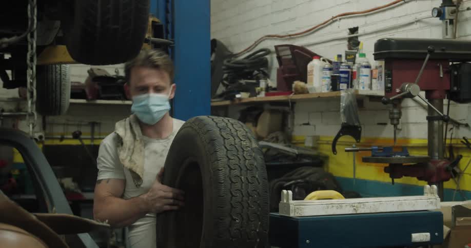 A mechanic picks up a tire inside a garage and carries it