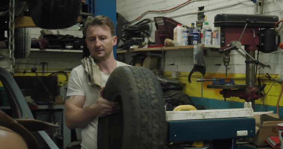 A mechanic picks up and carries a tire in a garage