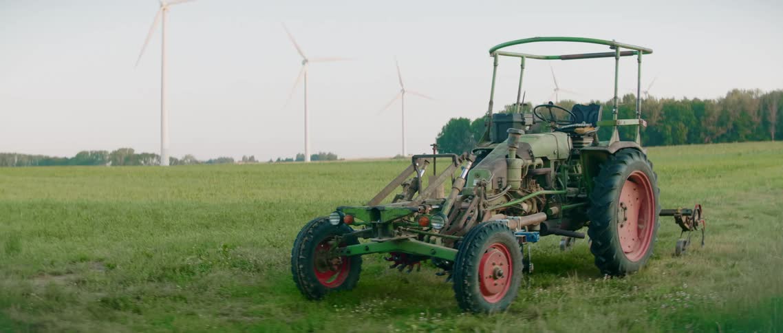 Tractor parked on field in front of spinning wind turbines