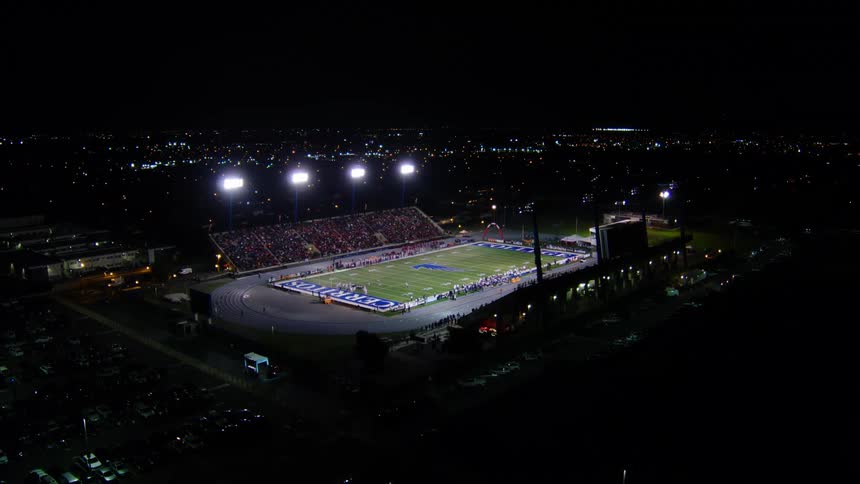 A football stadium with lights surrounded by streets and vehicles