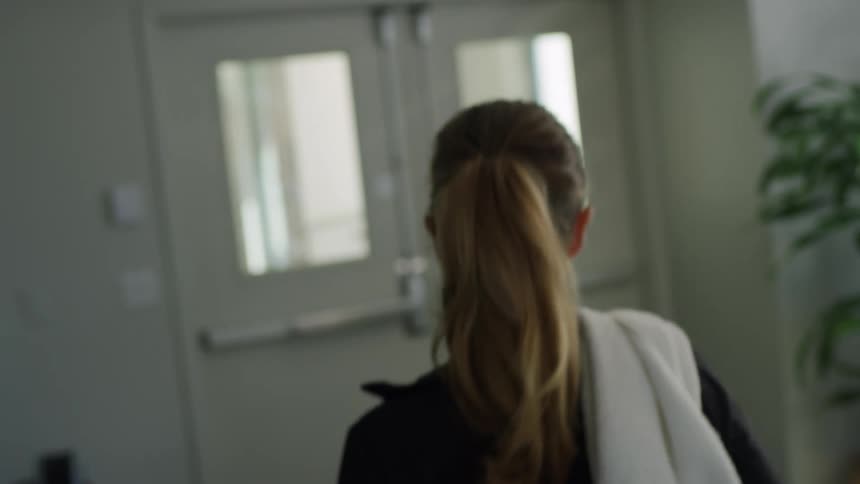 Woman throws towel over her shoulder and walk to door letting out into corridor