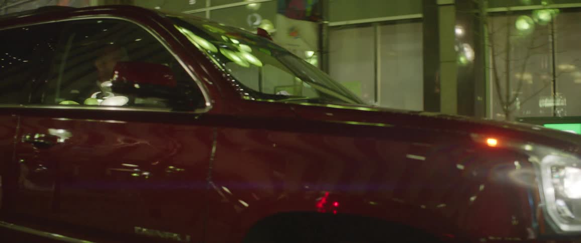 A woman drives her car with a male passenger down a city street at night
