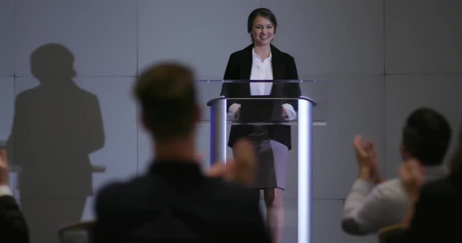 A woman leaves a podium after giving a speech with the crowd applauding her