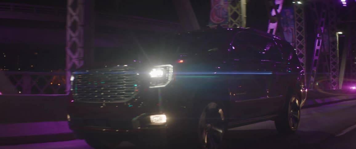 A car drives across a bridge with two people on it with the city skyline in the distance