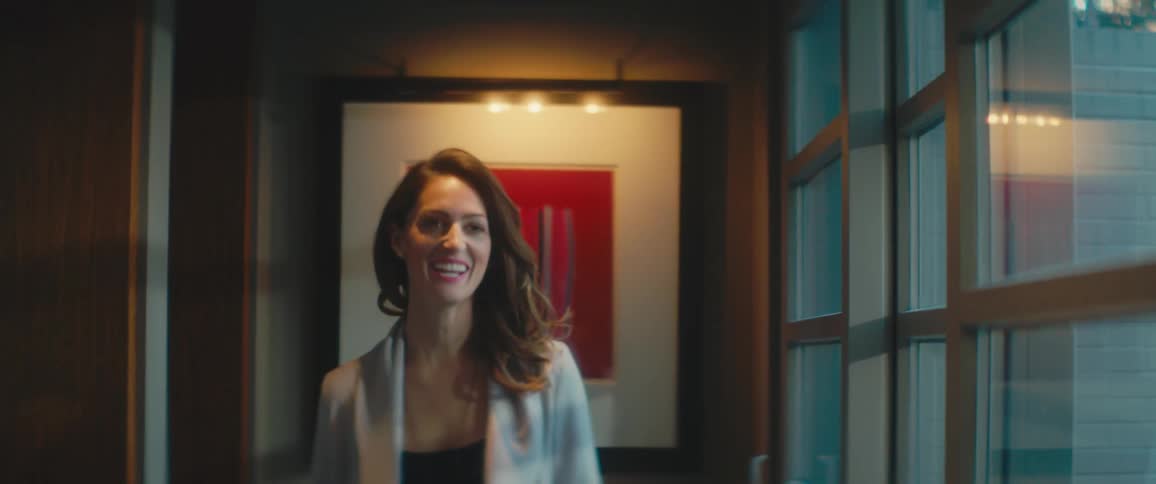 A woman smiles as she walks through a small corridor lined with windows