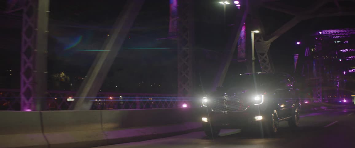 Large sport utility vehicle drives across bridge with purple lighting at night