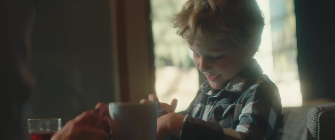 A woman holds a coffee mug as she sits at her kitchen table watching her young son play
