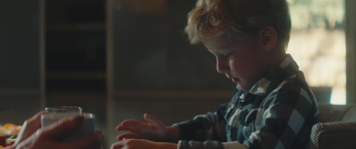 Blonde boy with a plaid shirt sits at a table and uses a tablet