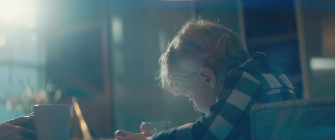A little boy sitting at a table with his mom looks confused as he uses a tablet