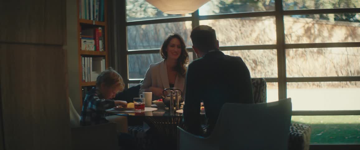 A family sits together at a small dining table with large windows behind them