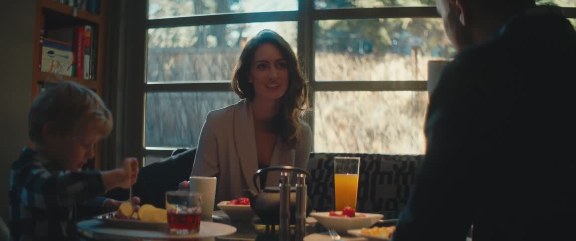 A woman smiles and nods while eating and drinking with her son and husband