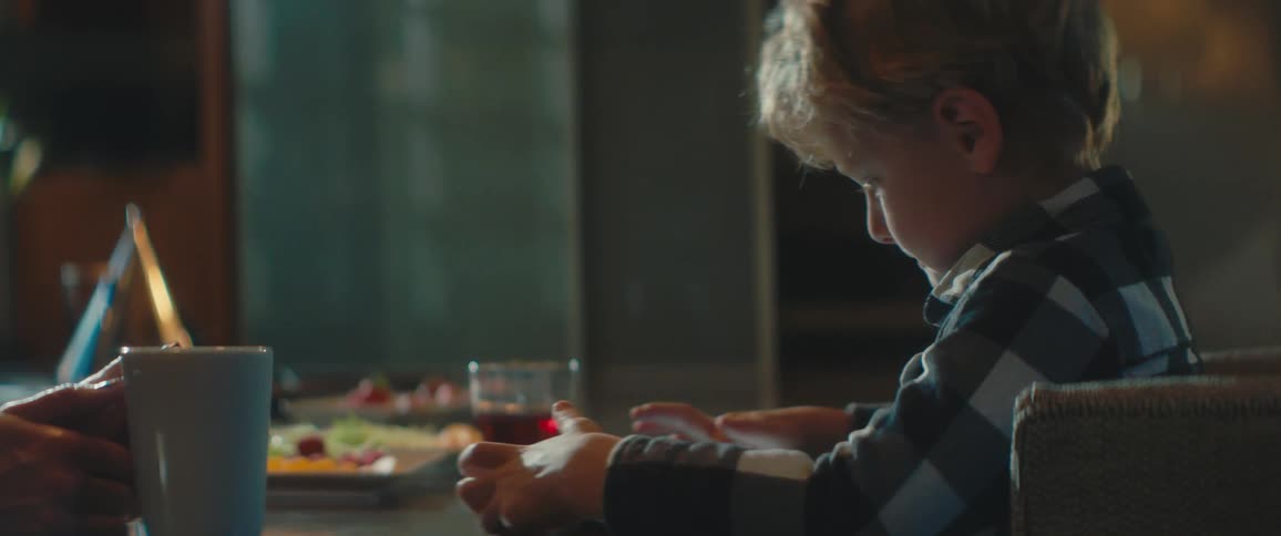 A little boy sits at a table with his mom and plays and smiles at her