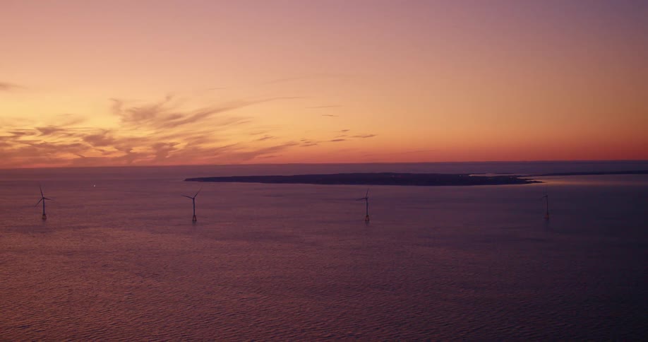 Aerial view of wind turbines in the ocean near an island at sunset