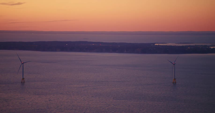 Wind turbines spin in the water off the coast at sunset