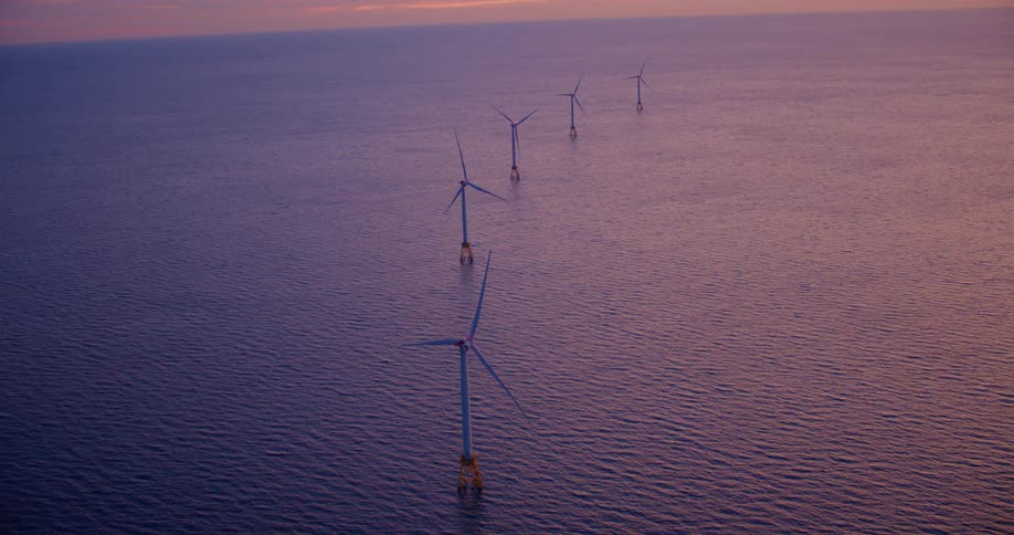 Aerial view of wind turbines in the sea off the coast at sunset