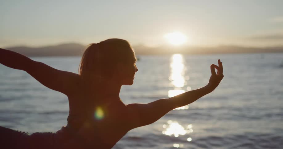 Silhouette of a woman practicing yoga next to a lake in the mountains at sunset