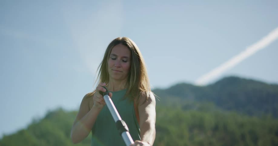 A woman stands on a paddle board and uses an oar to row