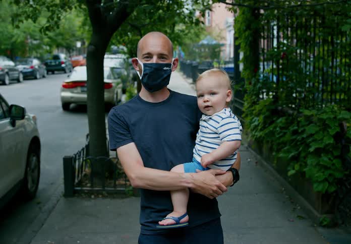 Father wearing face mask holds son on city sidewalk