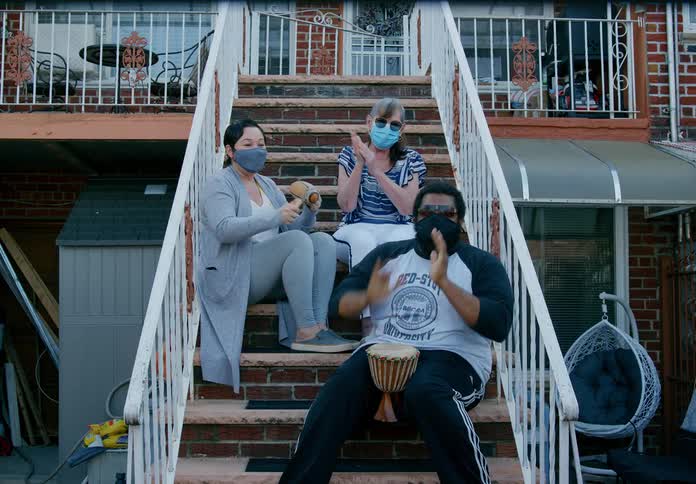 Three people sit on a building staircase clapping and playing small instruments