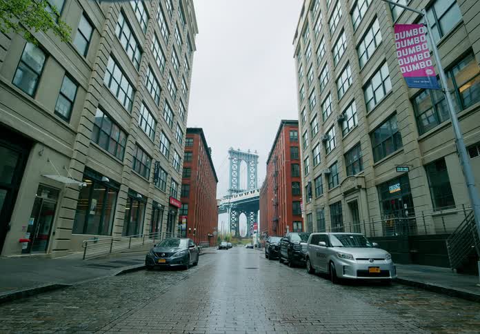 Cars parked on a city street with bridge visible behind and between buildings