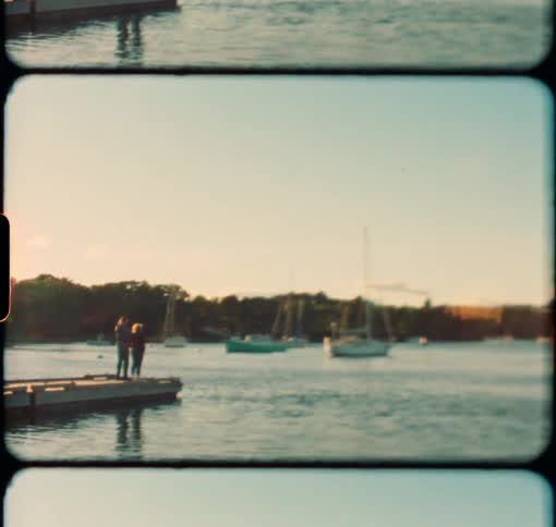 A couple stands at the end of a dock looking over the harbor at sunset
