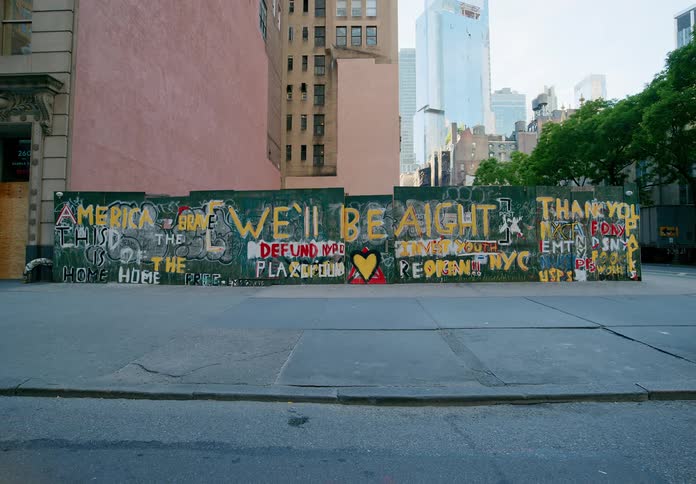 A city with a pavement and a wall with graffiti with a person walking by