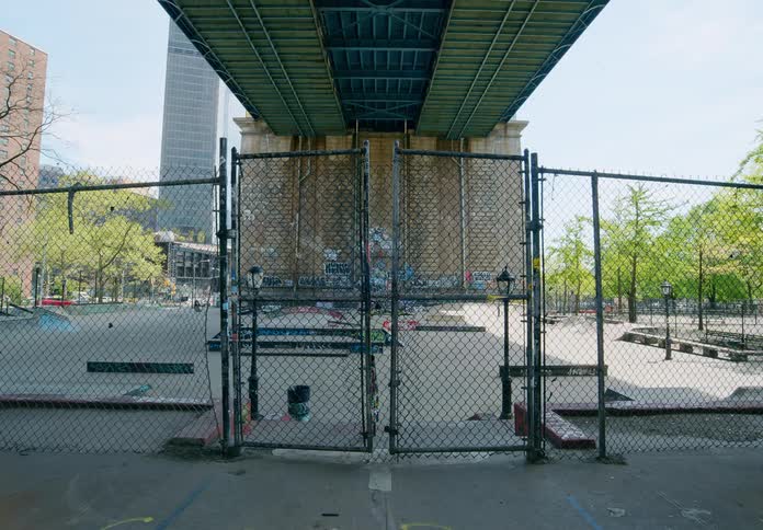 The locked gate of a chain link fence under a bridge in a metropolis during the day