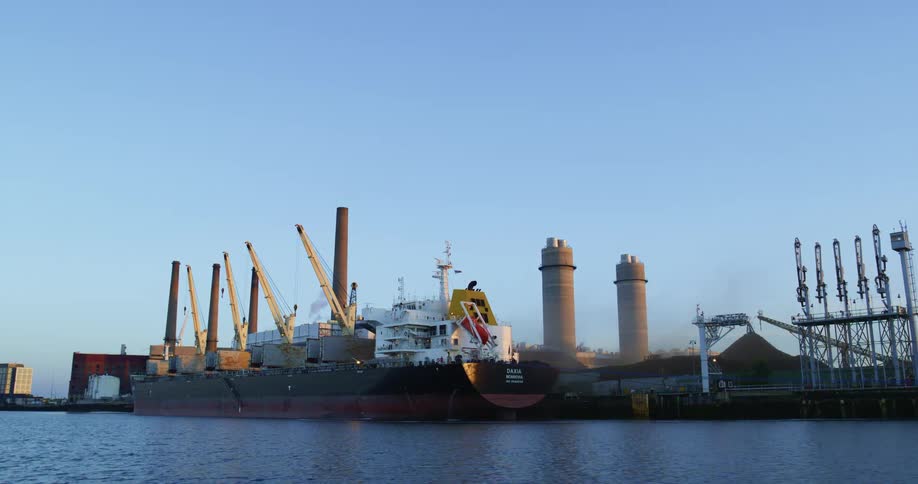 A shipping boat is docked at a refinery on the coast
