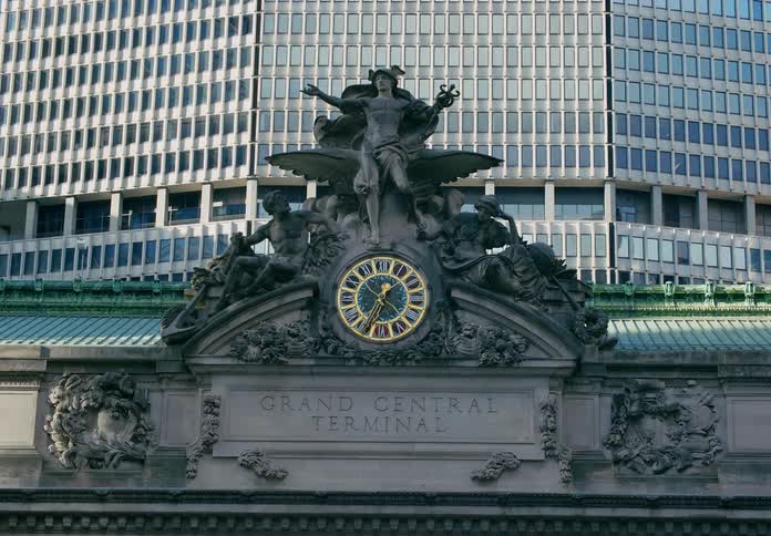 Clock and elaborate statue sit above building inscribed with the words grand central terminal