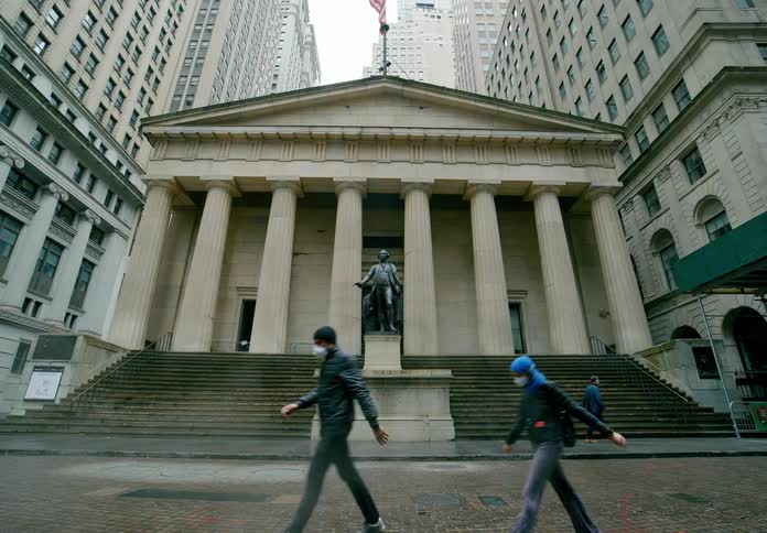 A building with a statue in front with people walking with masks