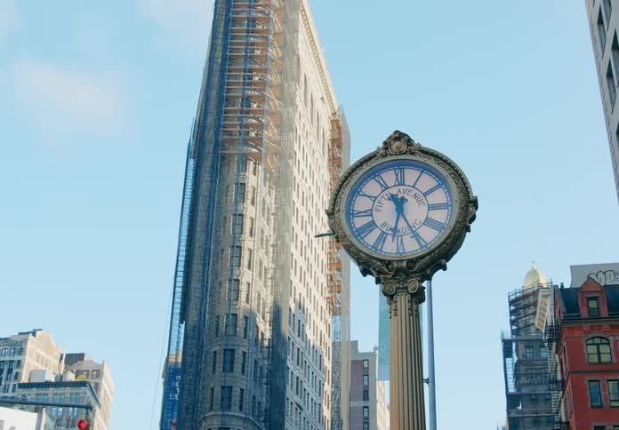 An analog clock atop a pole in metropolis on a sunny day