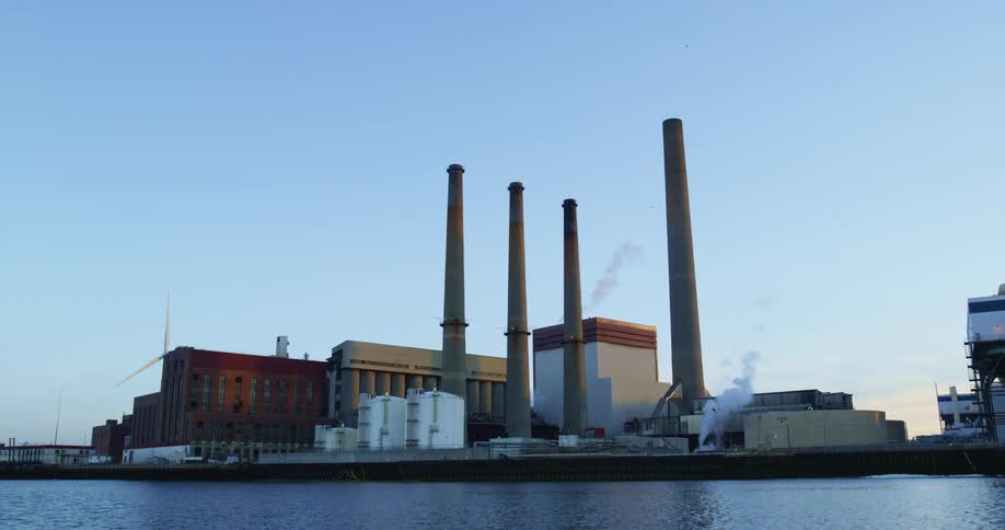 Tall smokestacks looming over a factory on the coast on a sunny day