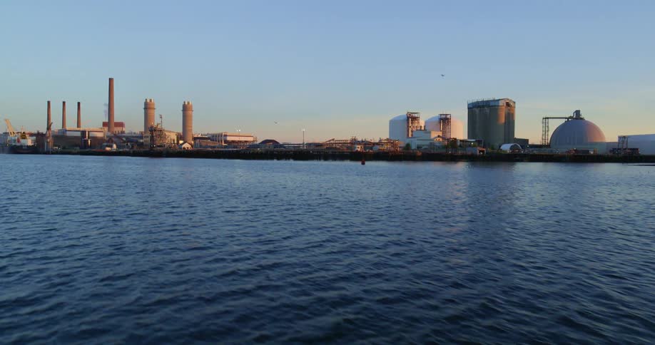 An ocean is displayed at dusk next to a power plant