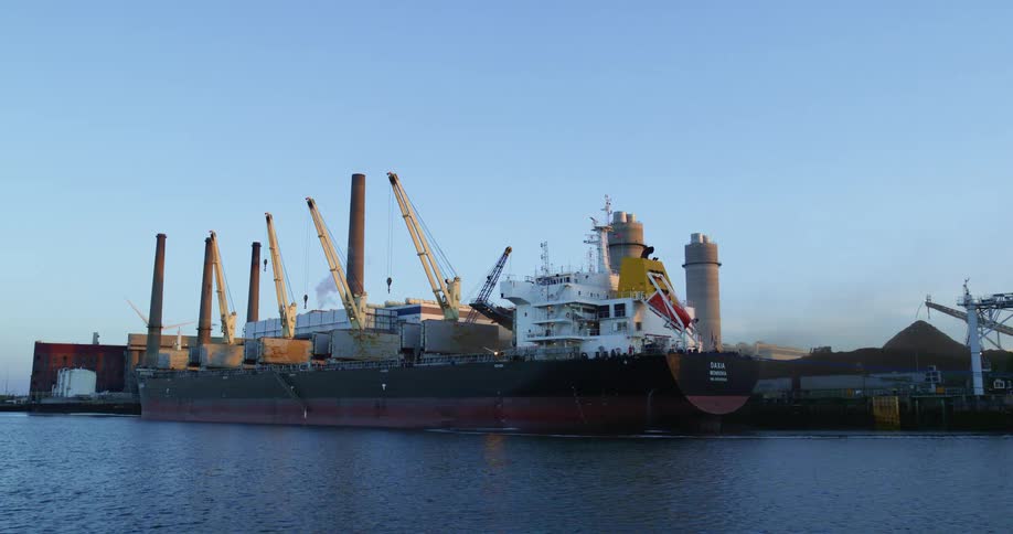 A large cargo ship is parked next to a ship yard with several cranes nearby