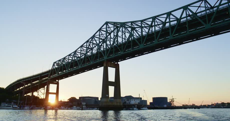 A bridge over a river with boats with the sky and sunset in the background