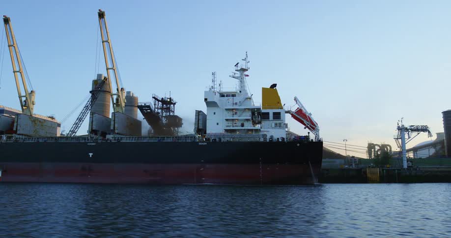 A large ship docked outside of a factory on a sunny day