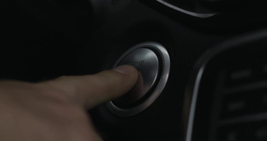A man uses his pointer finger to push the engine start button of an automobile