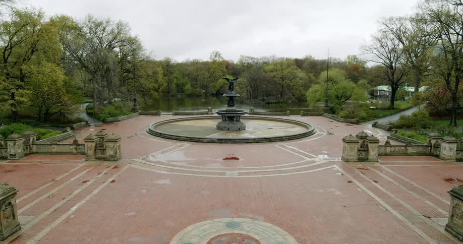 A disabled fountain in a large courtyard on the side of a lake on a cloudy day