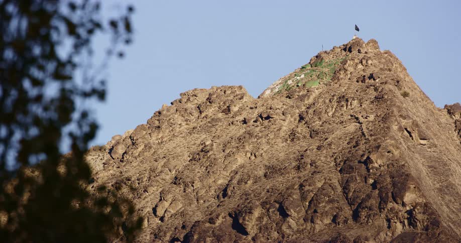 High atop a rocky and rugged mountain is a flag flapping in the wind