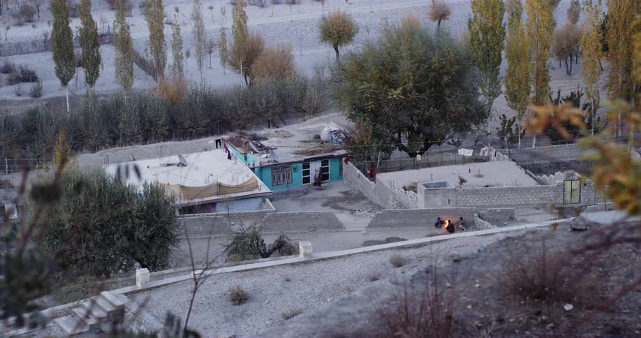 People sitting around a fire with buildings and trees in the background