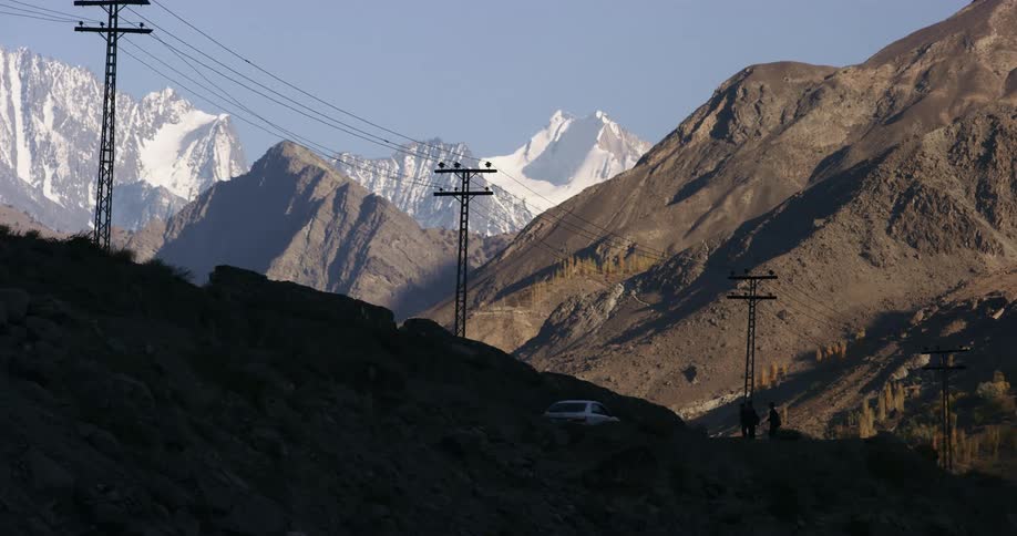 A car drives by people hitch hiking on the side of road in front of a mountain range