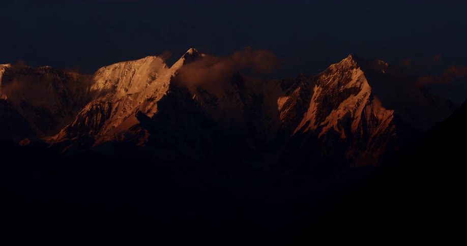 Time lapse of clouds hanging on the snow covered peaks of a mountain range from dusk to night