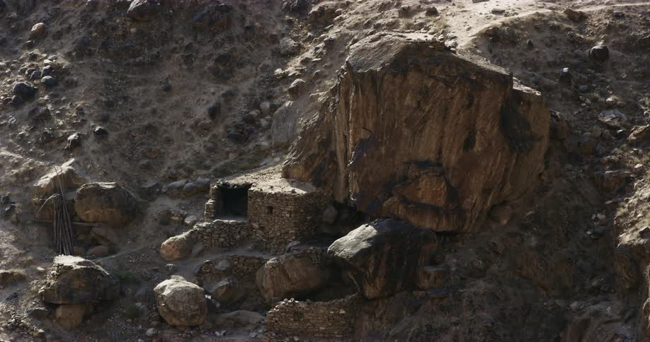 Primitive stone house near a giant boulder on the slope of a mountain