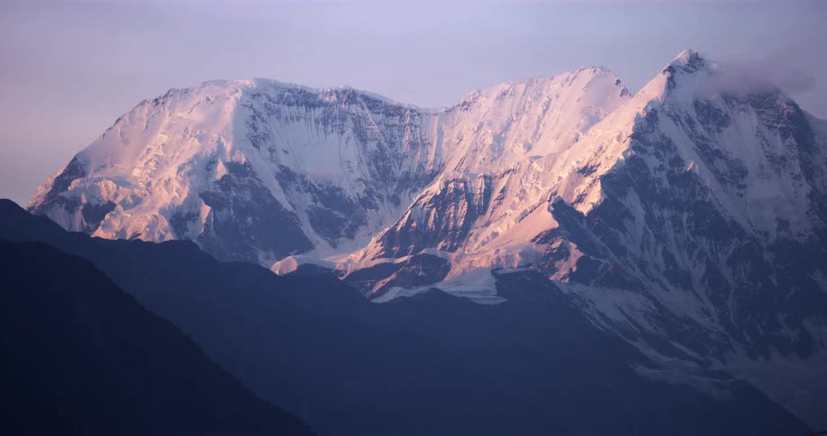 A large snow covered mountain range sits peacefully under beside a sunrise