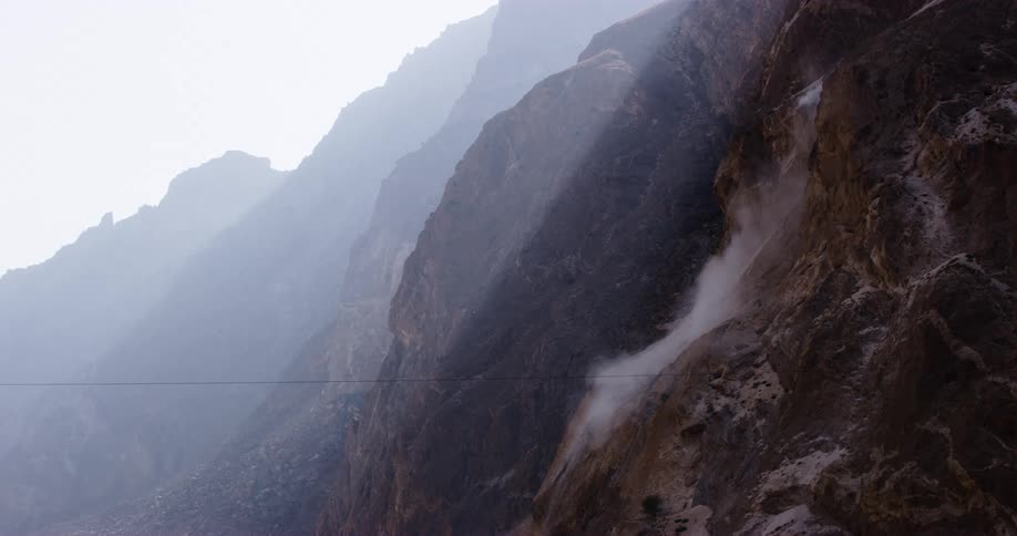 Mist and fog cling to the steep cliffs of a mountain range