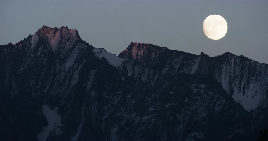 Moon rises above rugged mountain peaks