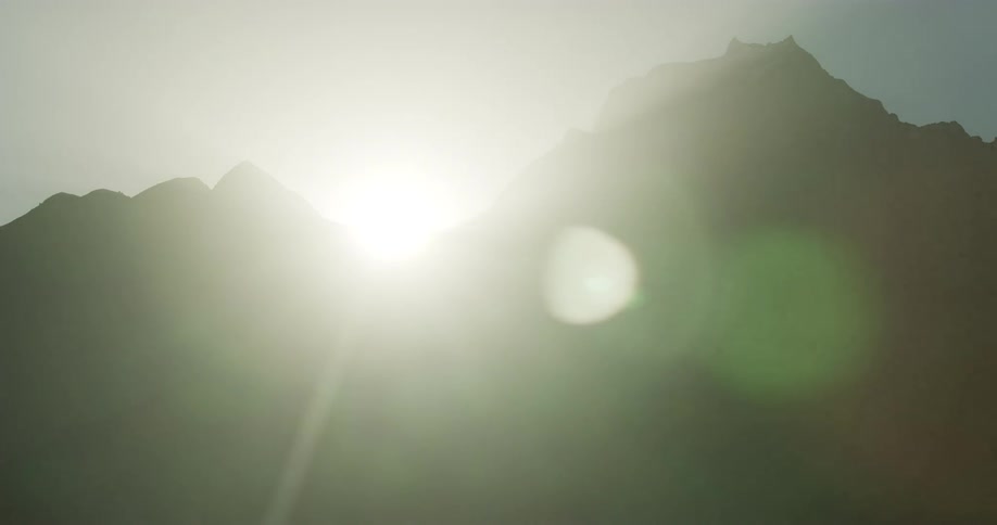 The sun rises between two peaks of a mountain range